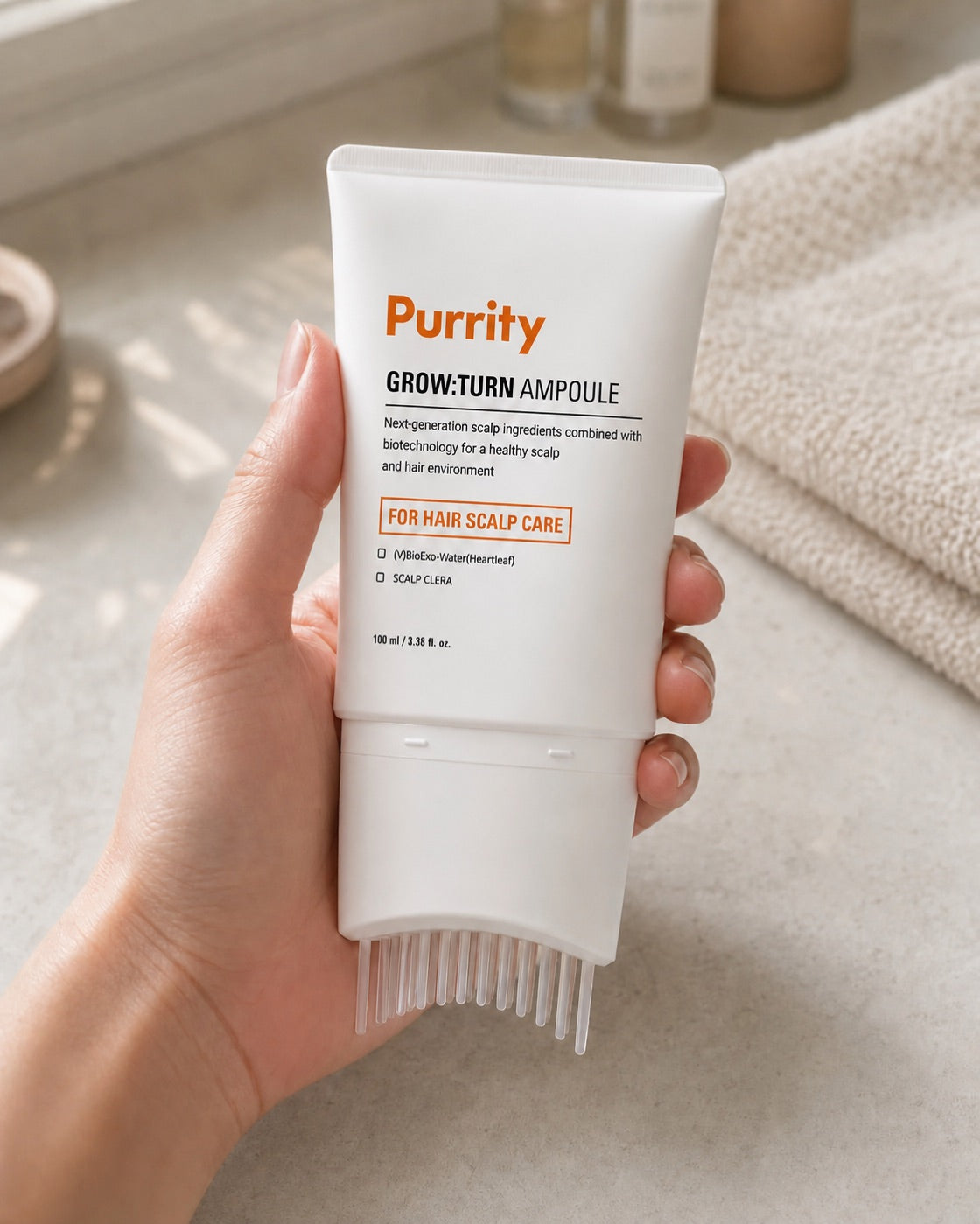 A hand holding the Purrity Grow:Turn ampoule on a bathroom counter, brush head down