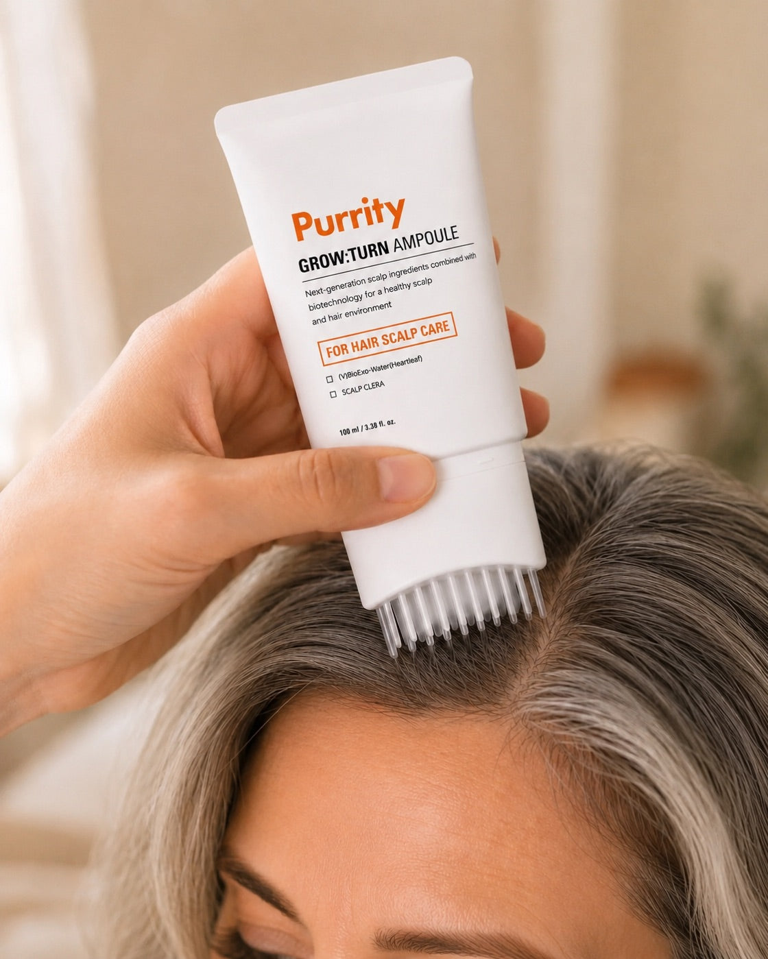 A hand pressing the Purrity Grow:Turn ampoule brush onto the scalp along the part line